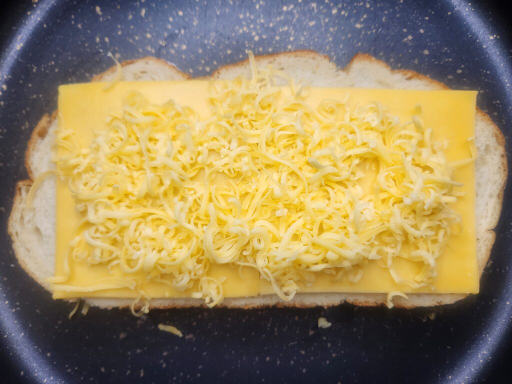 Place one slice of bread in hot pan and layer cheese on top for Sinful Grilled Cheese